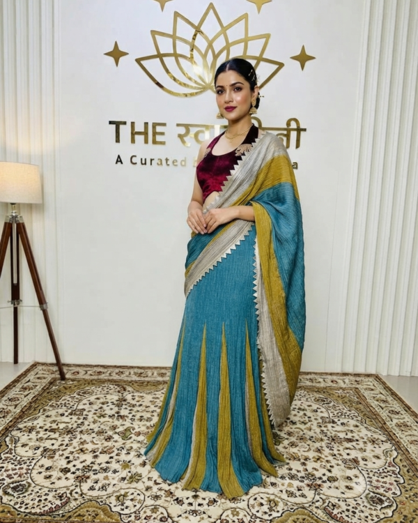 An Indian model wearing The Swamini by Sushmita's multi-shaded metallic blue, yellow, and beige flared skirt paired with a maroon velvet fish-cut blouse.