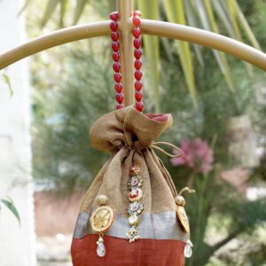 Shimmering tissue silk potli bag featuring an antique gold, silver, and rust color-blocked design with central Kundan stone work and a luxury red beaded handle by The Swamini by Sushmita.