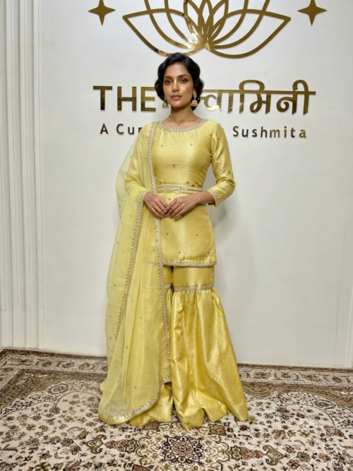 Indian model wearing a radiant yellow brocade fabric short kurti and matching garara paired with an organza dupatta by The Swamini by Sushmita.