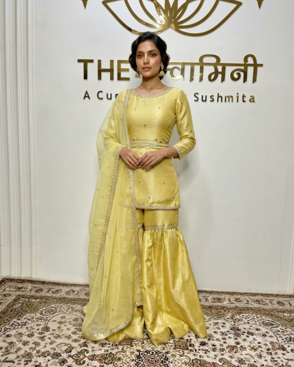 Indian model wearing a radiant yellow brocade fabric short kurti and matching garara paired with an organza dupatta by The Swamini by Sushmita.