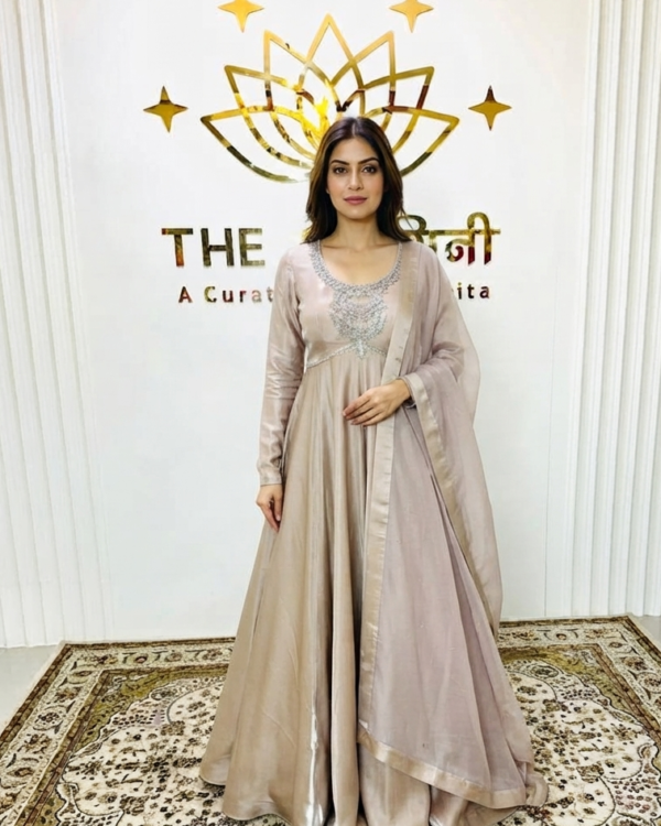Front-view product display of a floor-length soft golden Anarkali suit on a mannequin, featuring intricate silver embroidery on the bodice and a matching sheer dupatta, set against "The Swamini by Sushmita" branded background studio.