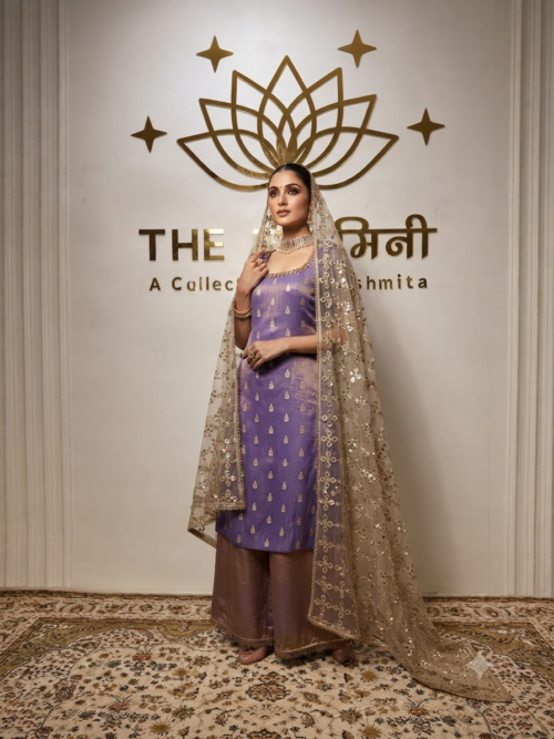 A woman in a lavender-violet Fenty silk suit with gold embroidery and a heavy gold-sequined net dupatta, posing in front of a branded wall.